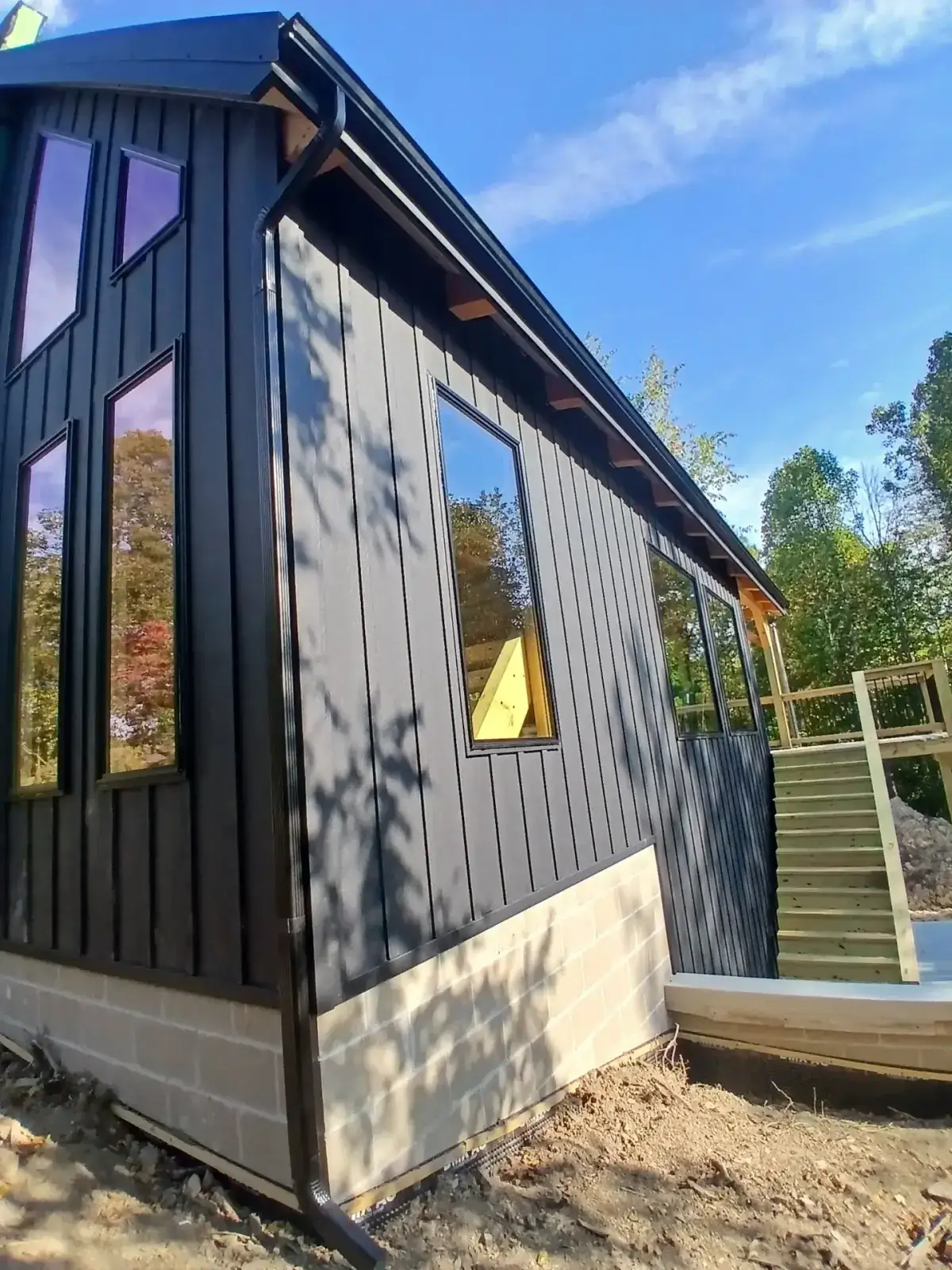 Black board and batten metal siding wrapped around a curved bay window wall beside a deck