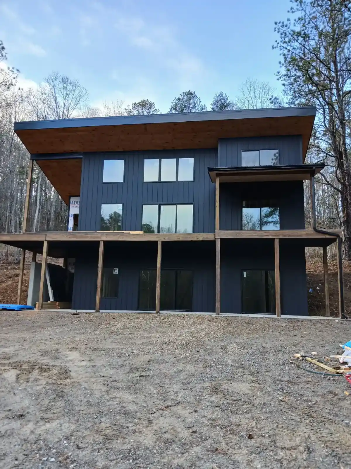 Modern three-storey hillside home clad in black board and batten metal siding with cedar soffits