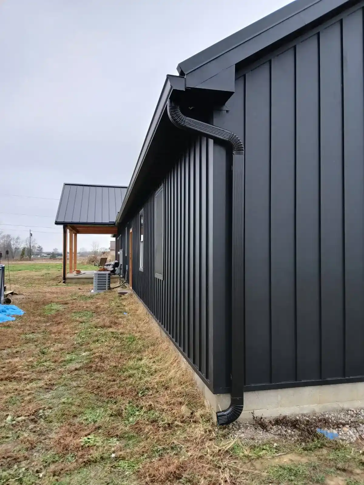 Black seamless gutter and downspout running the length of black board and batten metal siding