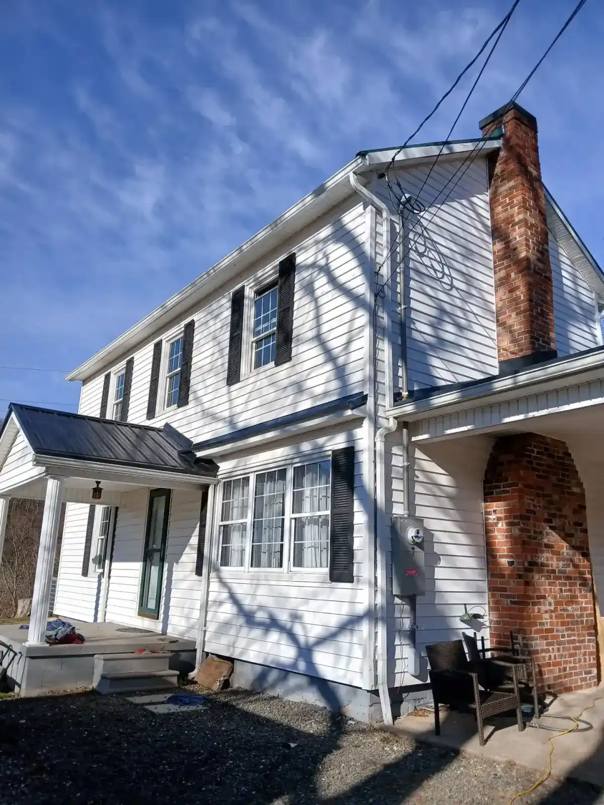 White farmhouse with a newly replaced black metal porch roof beside a brick chimney