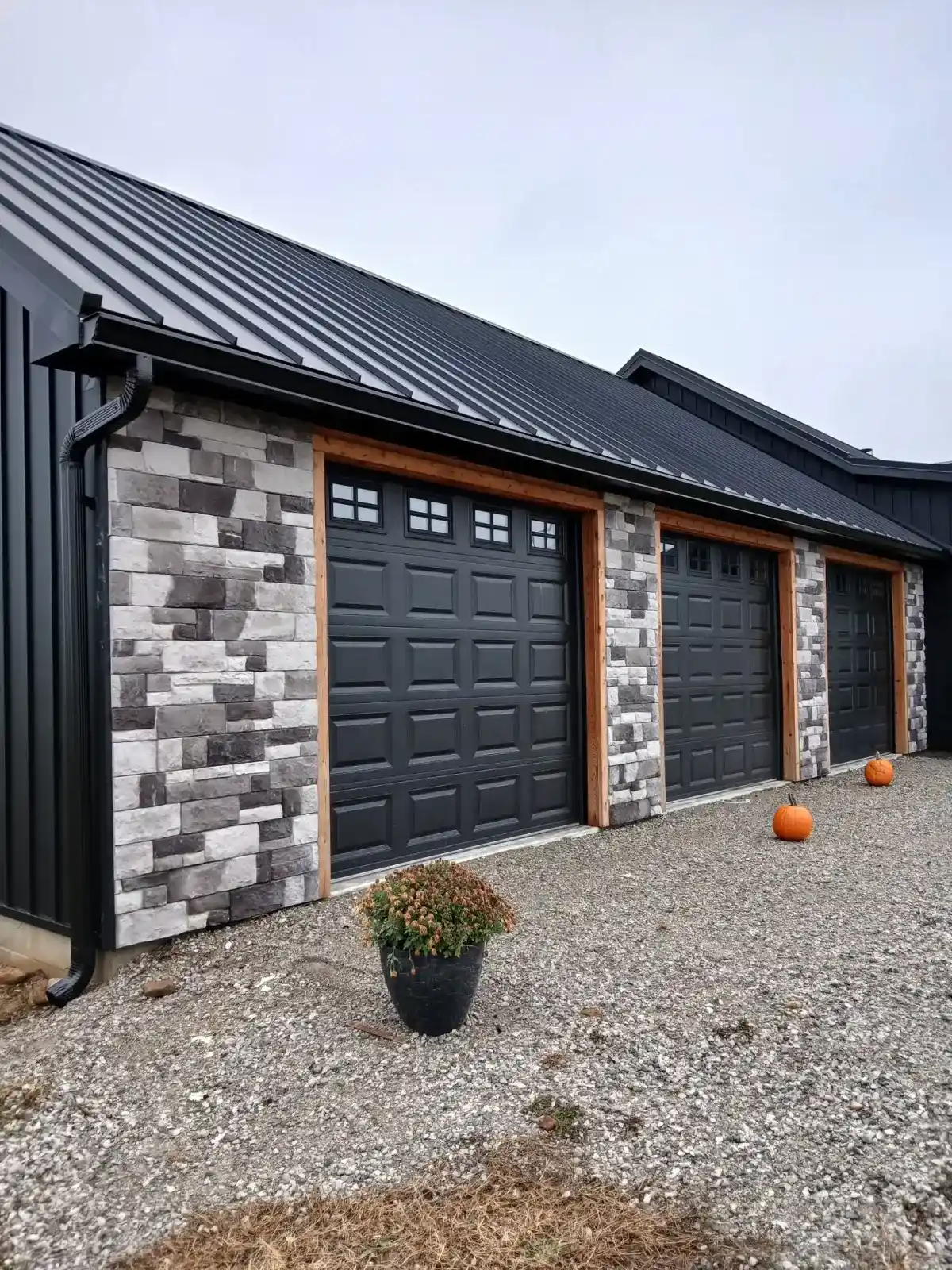 Black standing seam metal roof over a three-bay garage with stone columns and cedar trim