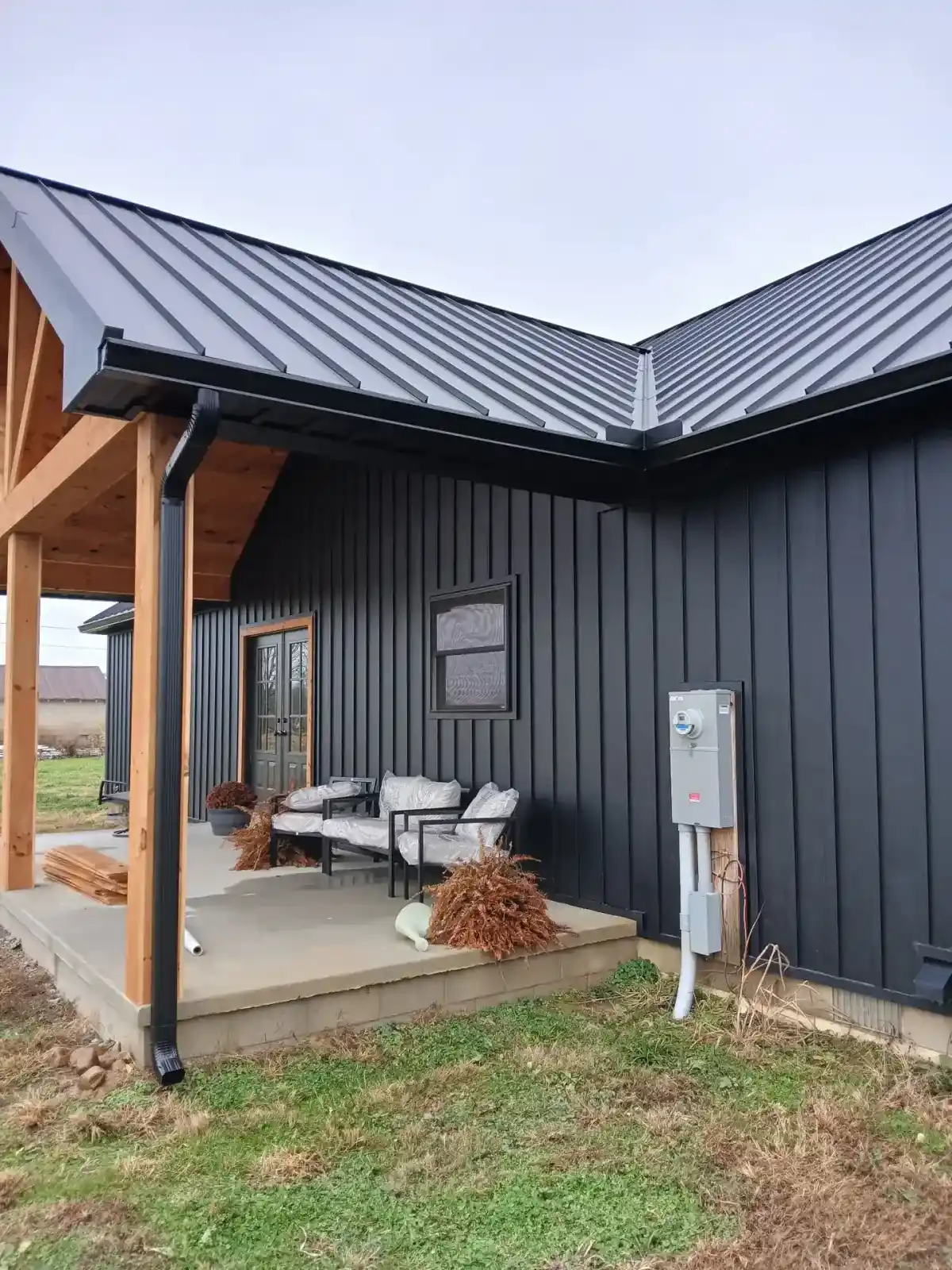 Corner of a black standing seam roof meeting metal siding above a covered porch