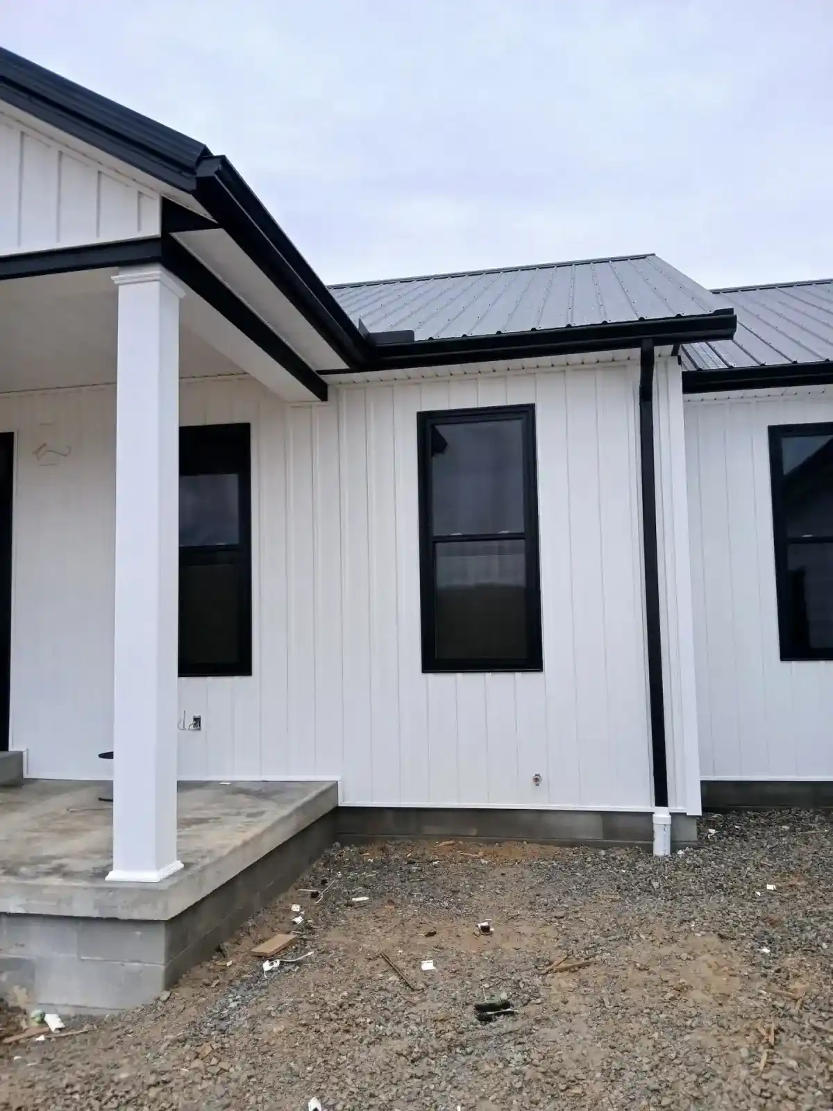 White board and batten metal siding with black metal roof and seamless gutters